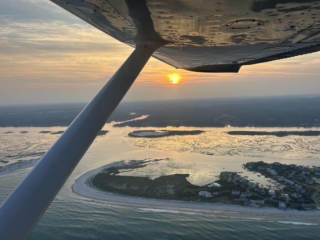 Sunset over a coastal inlet, seen past the wing strut of a high-wing trainer